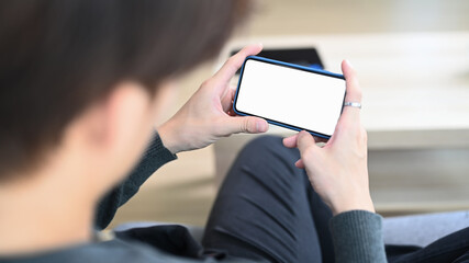 Close up view of casual man sitting on sofa and holding horizontal smart phone checking social media.