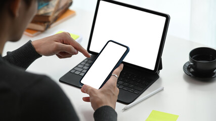 Cropped shot of young man working with computer tablet and using mobile phone.