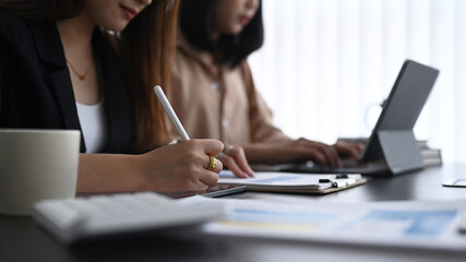 Two businesswoman analyzing business data on computer tablet and working together at office desk.
