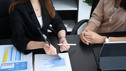 Businesswoman showing digital tablet to her colleague and discussing strategy for company growth in modern office.