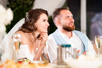 newlyweds sit at table in restaurant and listen to congratulations from guests.