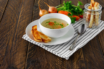 Chicken broth with parsley in a white bowl and croutons on a rustic wooden background.