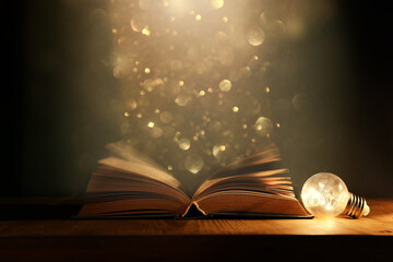 Magical image of open antique book over wooden table with glitter overlay