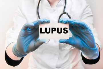 The doctor's blue - gloved hands show the word LUPUS - . a gloved hand on a white background. Medical concept. the medicine