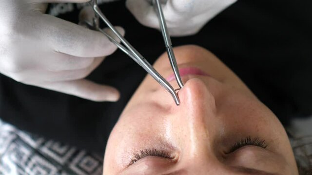 Body piercing process. Professional piercer in the disposable gloves sets nose ring properly 