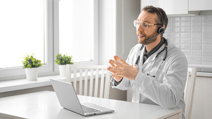 Photo of a doctor in front of a laptop monitor. He advises the client on video communication. Format 16:9.