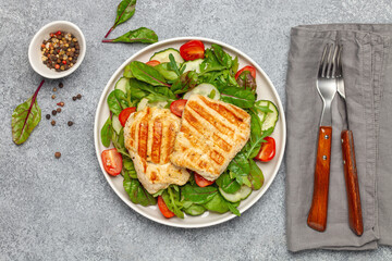 Fresh salad - cucumbers, tomato, arugula, chards leaves and chicken fillet grill in a plate on the table. Top view. Healthy diet food.
