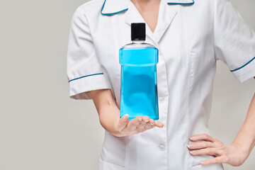 woman dentist doctor holding bottle of mouthwash standing over grey background