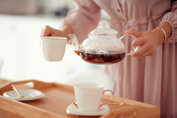 a girl in a pink dress pours tea from a teapot into a white cup on a blurry background