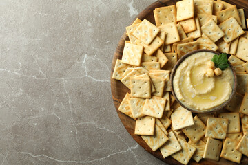 Tray with crackers and bowl of hummus on gray background