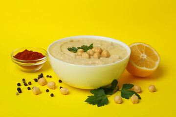 Bowl of hummus and ingredients on yellow background