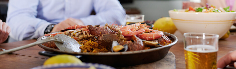 Crop people at table with paella dish