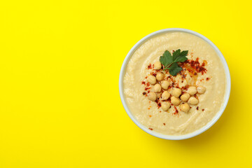 Bowl of fresh hummus on yellow background