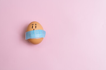 Egg covered with blue medical face mask. On pink plain background. Pandemic Easter season, creative idea concept. Copy space for text, closeup