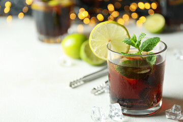 Glass of Cuba Libre on white textured table against blurred lights