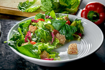 Mix salad with salmon, cherry tomatoes and avocado, served in a white plate on a dark marble background. Restaurant food.