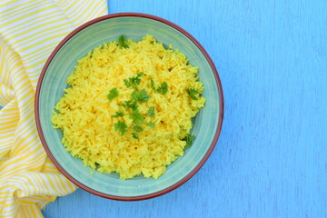 Indonesian yellow turmeric rice or Nasi Kuning in a bowl garnish with chopped parsley. Blue background
