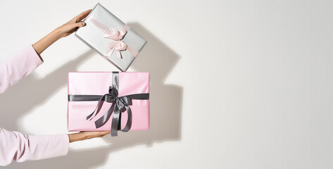 Obraz premium Womens day celebration. Female hands holding two wrapped gift boxes against light background with shadow. panoramic banner with copy space for text