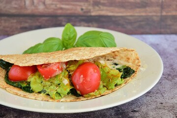 Whole wheat tortilla wrap filled with avocado, spinach and tomato garnish with basil leaf
