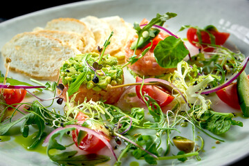 A French starter before the main course - salmon steak tartare with avocado, cherry tomato and croutons, served in a white plate. Restaurant food. View from above