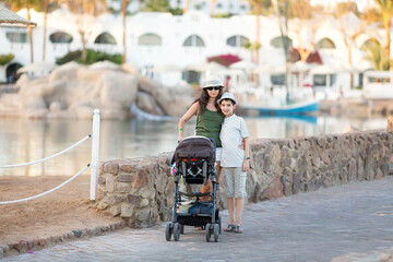 Summer portrait of woman.  Family vacation. Holiday. Summer landscape. Young mother and her son with a baby carriage.