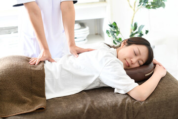 ベッドでマッサージ（整体）を受ける若い女性