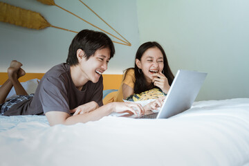 excited couple laughing on bed using the laptop at home in the bedroom together