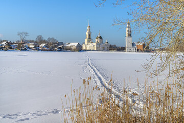Fototapeta na wymiar Winter in the ancient city of Nevyansk (Russia). A view from the frozen city pond to the historic center with its famous leaning tower and a majestic temple. Pure white snow, path and blue sky