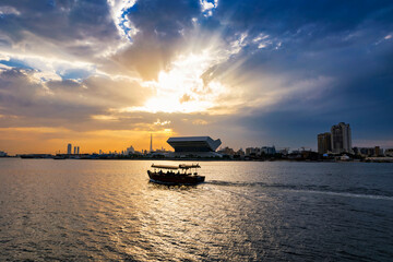 Beautiful view of Dubai Skyline in the evening. A boat or water taxi in the foreground. Dubai city during golden hour or sunset with beautiful cloudy sky.