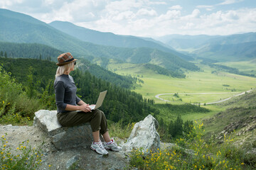 Fototapeta premium Beautiful woman hipster traveler freelancer with laptop on the top of the mountain. Remote work concept.