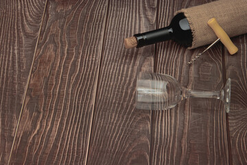A bottle of expensive red wine with a glass and a corkscrew lie on a background of wooden boards