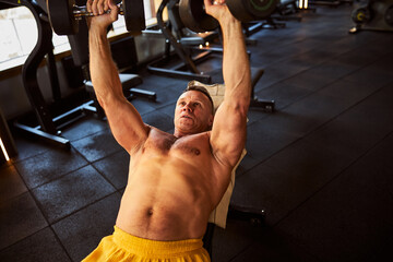 Fototapeta premium Focused man with bare torso using dumbbells at gym