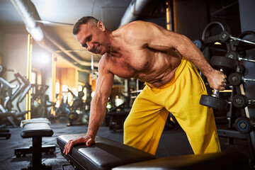 Fototapeta premium Gladsome sportsman using dumbbells for gym workout