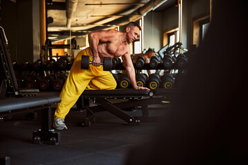 Focused male athlete holding dumbbells and leaning on bench