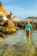 Woman wading into natural rock pool in early morning light