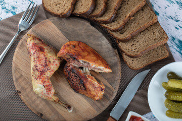 Delicious fried chicken parts on wooden plate with pickles and bread slices