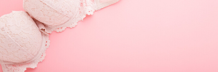 Adult female lace bra on light pink table background. Pastel color. Closeup. Wide banner. Empty...