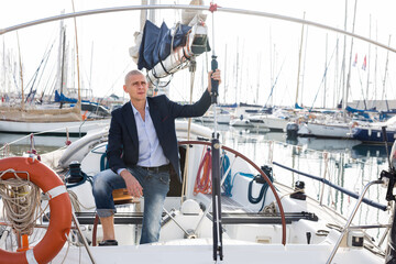 European man in jeans and a jacket posing on yacht in port