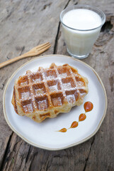 Waffles in a plate and Milk are placed on the wooden table.