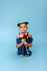 cute happy little girl holding bouquet of pink roses on blue background.