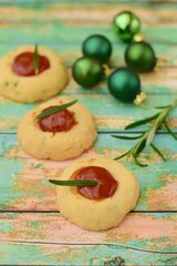Homemade rosemary thumbprint cookies with jam on green wooden background. Decorated with Christmas green balls. Selective focus
