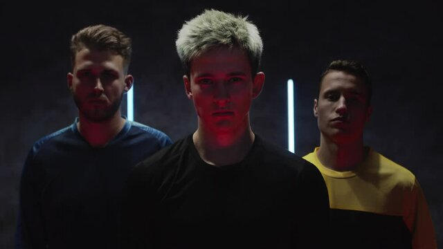 Young caucasian male athletes sportsmans posing against bright lights in a dark studio. Football team. Soccer amateur players. Portrait in slow motion. Sport. Shot on Blackmagic in ProRes. Bet