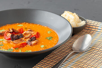 Tom Yam Thai soup in black bowl on gray table