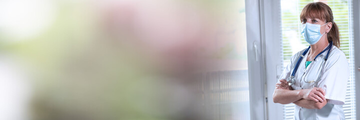 Female doctor with arms crossed wearing a face mask; panoramic banner