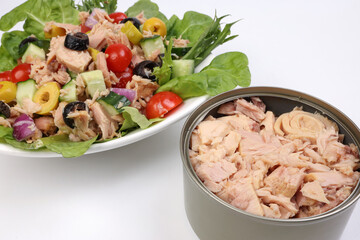 Tuna fish meat salad cucumber tomato onion black green olive leaf lettuce on white plate tuna flake chunk in tin can over white background