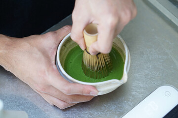 Barista Using bamboo whisk (chasen) stir matcha and hot water in the bowl on table, Mixing green...