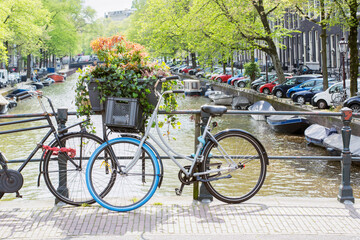 Fototapeta na wymiar Two Dutch bikes are standing on the bridge on the spring day in Amsterdam. Typical spring Dutch landscape with standing bikes near the canal