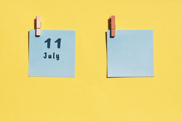 July 11st. Day of 11 month, calendar date. Two blue sheets for writing on a yellow background. Top view, copy space. Summer month, day of the year concept