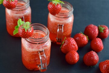 Fresh organic strawberry smoothie with mint in glass jar on black background