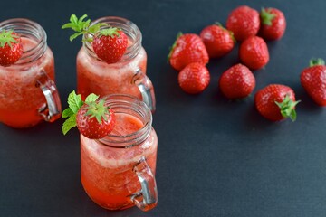 Fresh organic strawberry smoothie with mint in glass jar on black background
